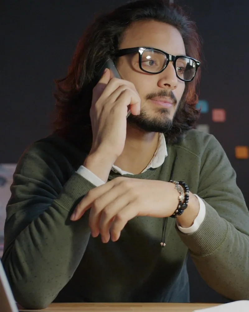 A man on a phone call at his desk, laptop open