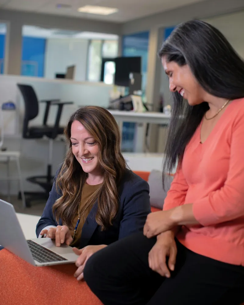 Two colleagues smiling as they review work on a laptop